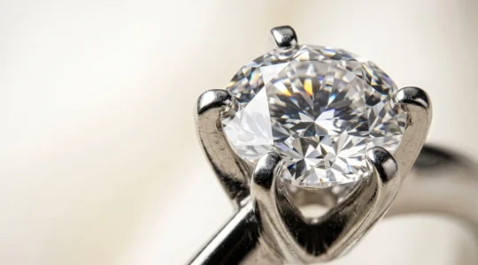 Gros plan sur un diamant brillant serti de griffes fines en métal précieux, illustrant le compromis entre luminosité maximale et sécurité du sertissage pour une bague de fiançailles